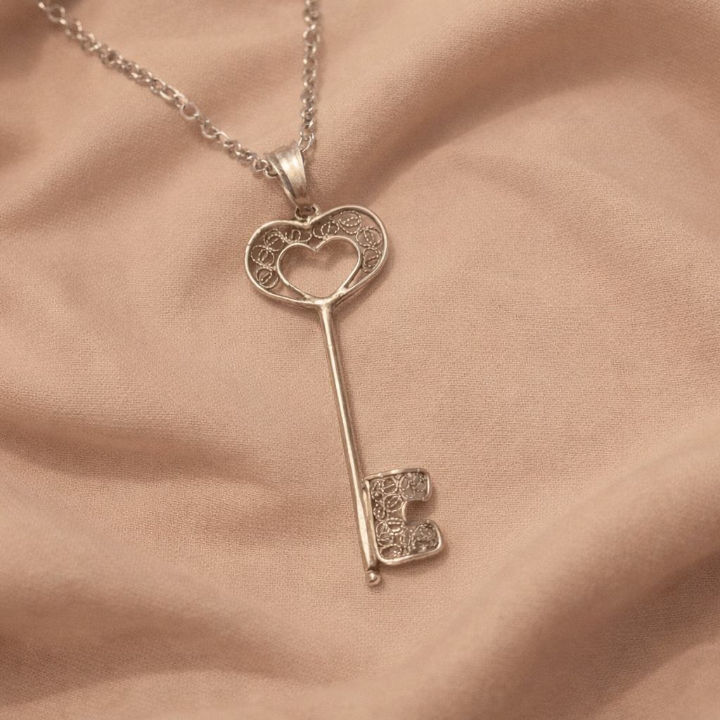 Silver key-shaped pendant necklace on a soft pink fabric background